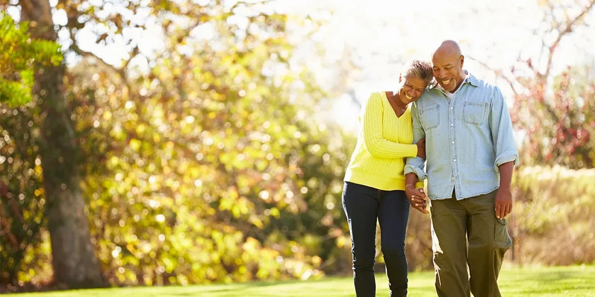 An older couple walking arm in arm outdoors on a bright day.